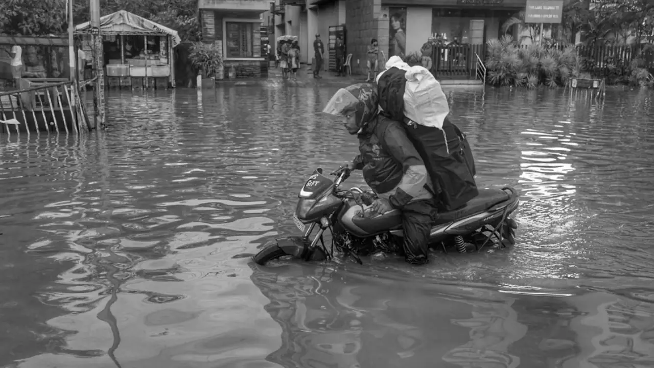 Mumbai commuters navigate a waterlogged road during heavy monsoon rain, as schools and colleges remain closed.